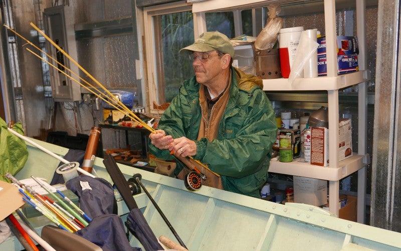 Artist wearing a green jacket and green hat putting fly-fishing gear into his fishing boat.