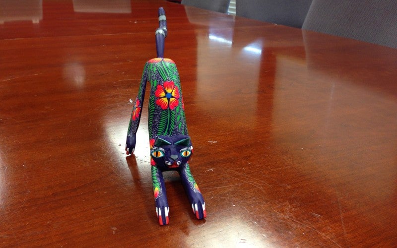 A dark blue cat figurine in a stretching pose and painted with floral and plant imagery.