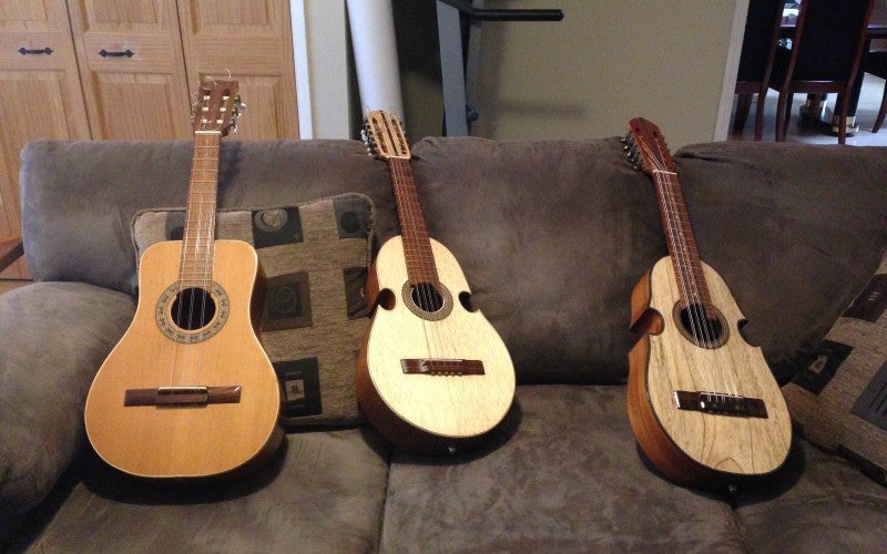 Three tan guitars sit on a gray couch.