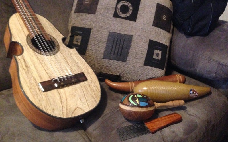 Four various wooden items sit next to a guitar on a gray couch, including a painted maraca.