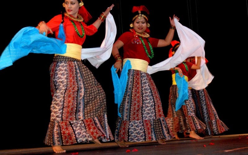 Three women dance on a stage wearing traditional dance dresses and hair pieces.