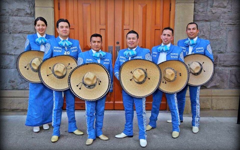 Members of José's mariachi band stand wearing blue outfits and hold wide-brim tan sombreros.