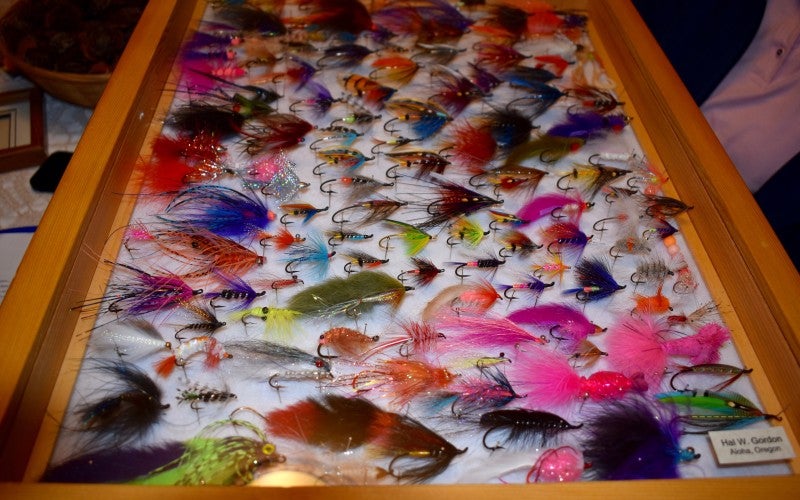 A wooden drawer filled with fly fish hooks of various sizes and colors.