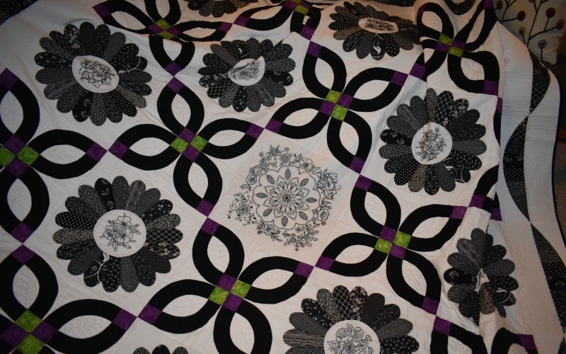 A white, black, green, and purple flower quilt.