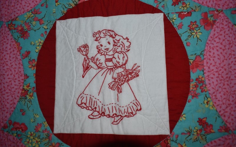A quilt square depicting a young girl wearing a dress and holding flowers.