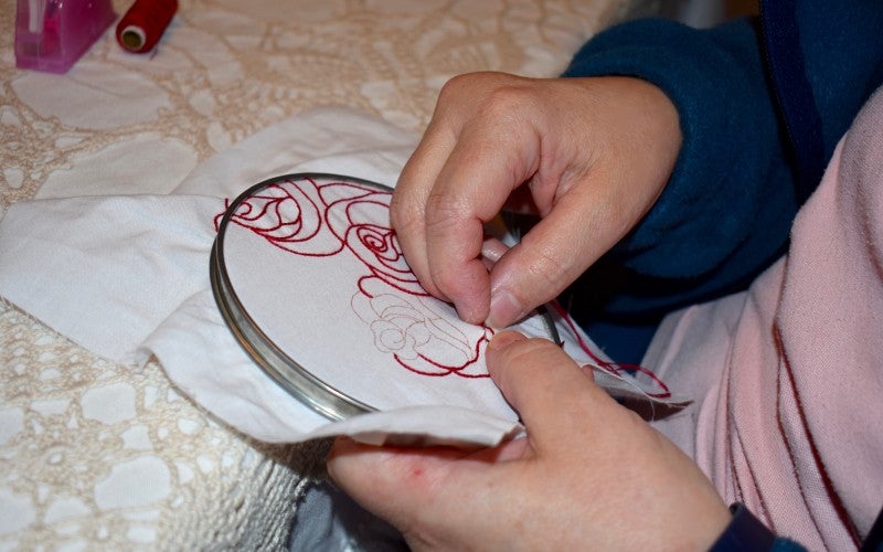 Jean embroiders rose imagery with red thread on a white cloth.