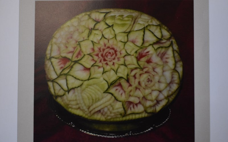 A green and pink watermelon carved with intricate flower designs.