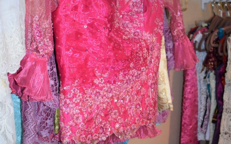 A pink three-quarter sleeve shirt hangs on a rack. It is decorated with flower details and the sleeves are made of a sheer material.