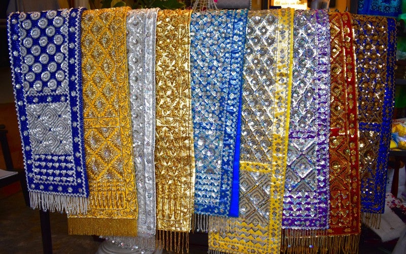 Various tapestries are hung over a rack. They range in color, including blue, yellow, and silver.