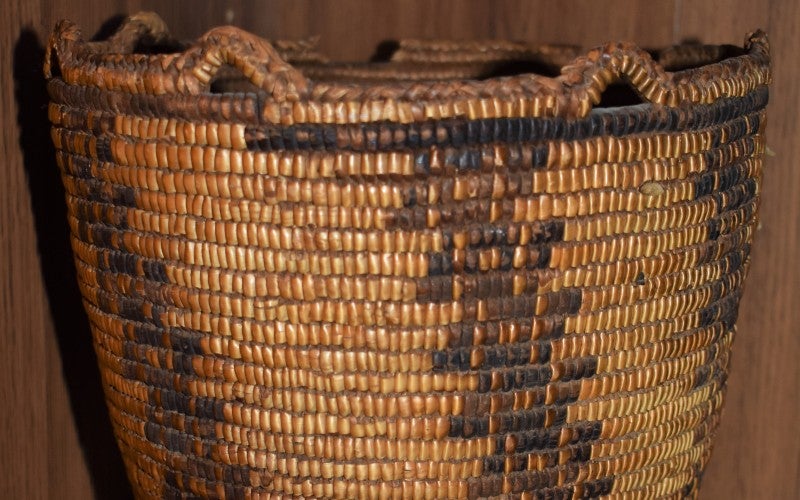 A tan and dark brown woven basket handcrafted by Celeste.