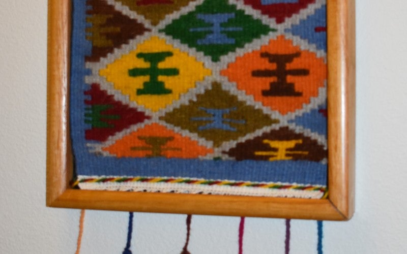 A hanging woven rug with a rectangular blue, red, orange, yellow, green, and brown pattern.