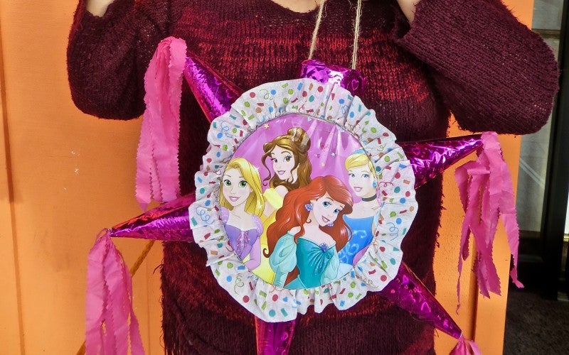A pink piñata featuring the Disney princesses Rapunzel, Belle, Ariel, and Cinderella. The piñata has five cone-shaped points.