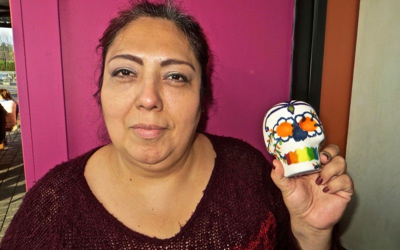 A small sugar skull decorated with orange eyes, a rainbow mouth, and blue, orange, and green plant designs.