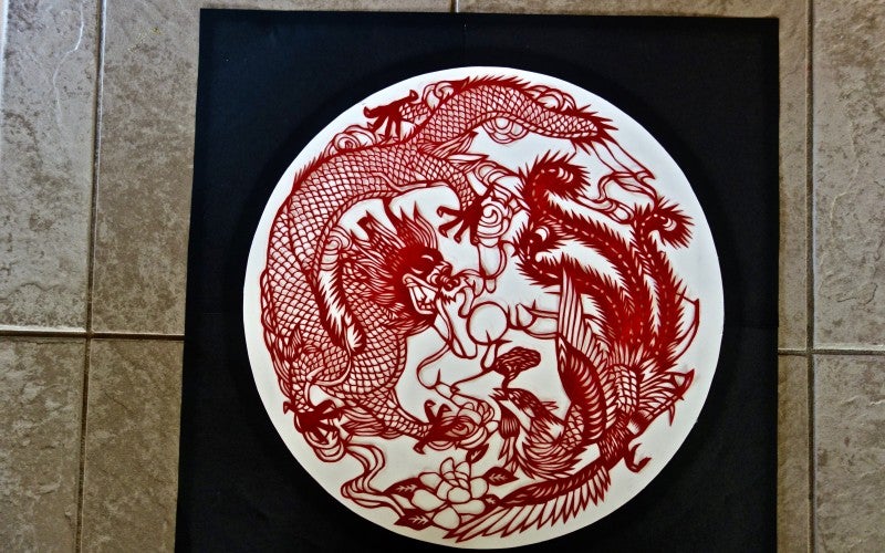 A circular white piece of cardboard with an intricately crafted red paper overlay depicting a dragon.