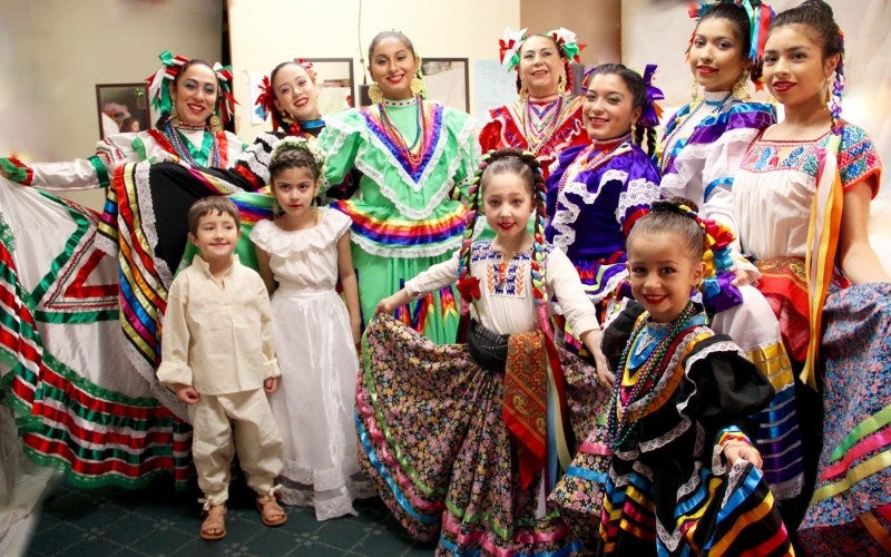 A group of women and young girls wear ballet folklorico dresses.