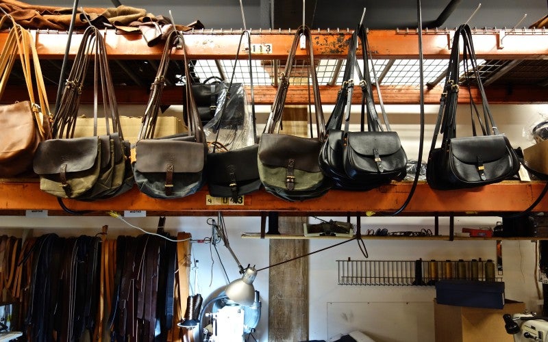 Multiple leather bags hang from hooks in José's workshop.