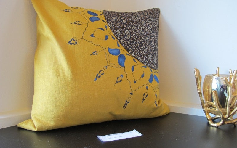 A yellow pillow with a blue paisley design in one corner.