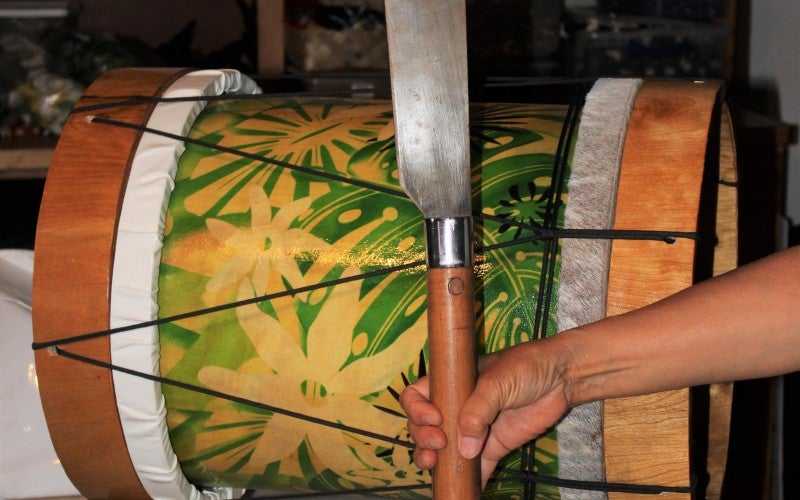 Someone holds a large paddle next to a green drum