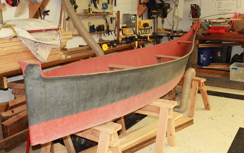 A red and black canoe in Brian's workshop, with tables of tools in the background.