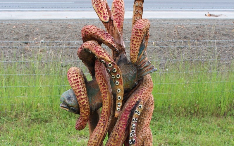 A wood sculpture of a fish being held by octopus tentacles.