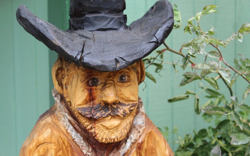 A wood sculpture of a man who has a mustache and wears a black cowboy hat.
