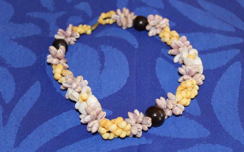 Shell necklace with white, pink, and yellow shell bunches interspersed with black round beads.