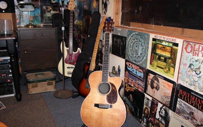 Three guitars sit inside a music studio, with various album covers decorating the wall.