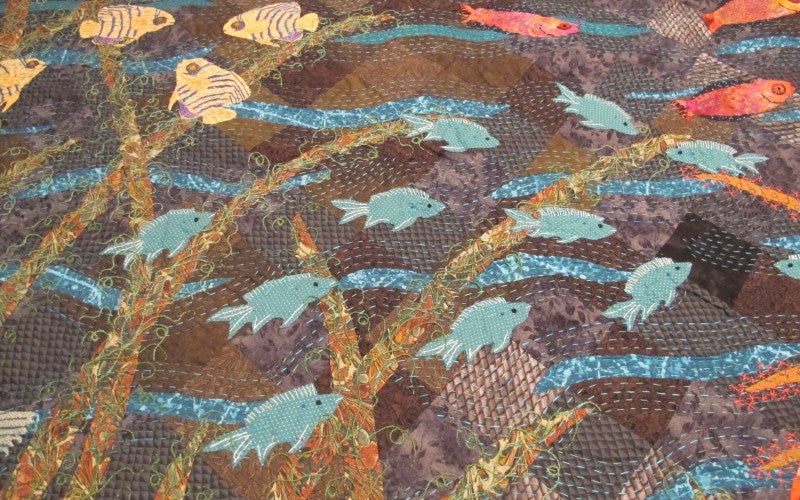 A multi-colored ocean themed quilt with blue, yellow, and red fish.