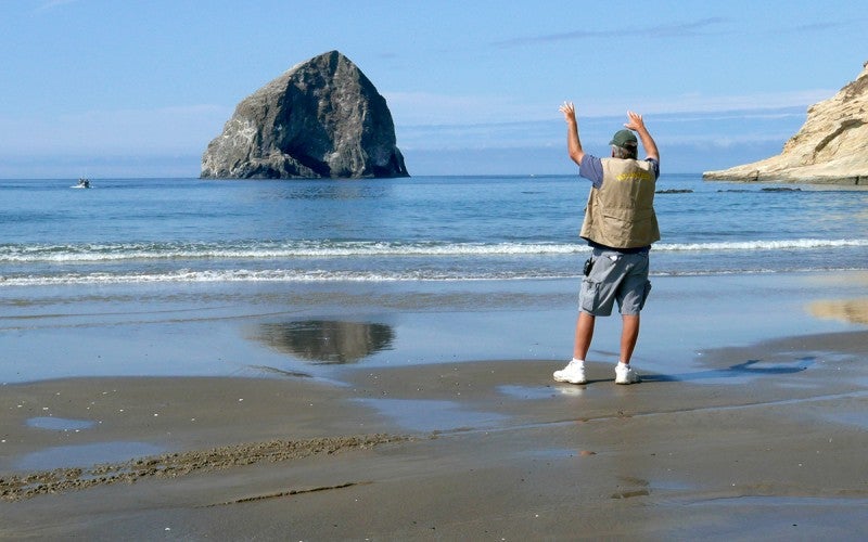 A man standing on a beach signals to a boat in the ocean