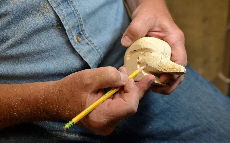 Rick Pass draws on part of a wooden duck decoy with a pencil