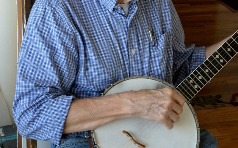 Hobe plays a banjo and wears a blue shirt.