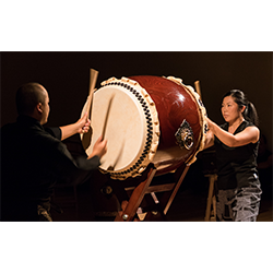 Two people play both sides of a large taiko drum