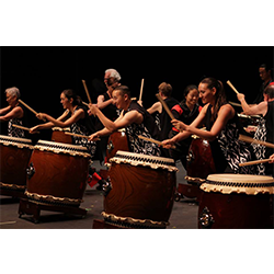 A group of people play taiko drums together on a stage