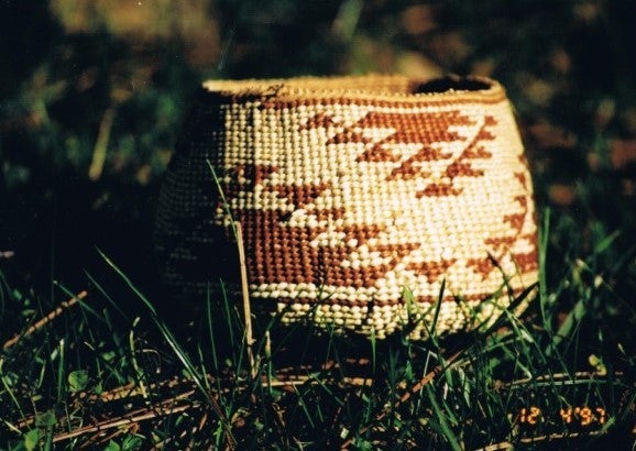 A white basket with brown geometric patterns sits in grass