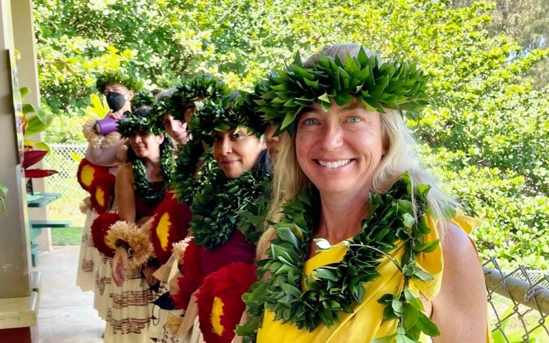 Andrea Luchese wearing yellow shirt and leaf leis. She is holding a hand drum and standing in line with her students.