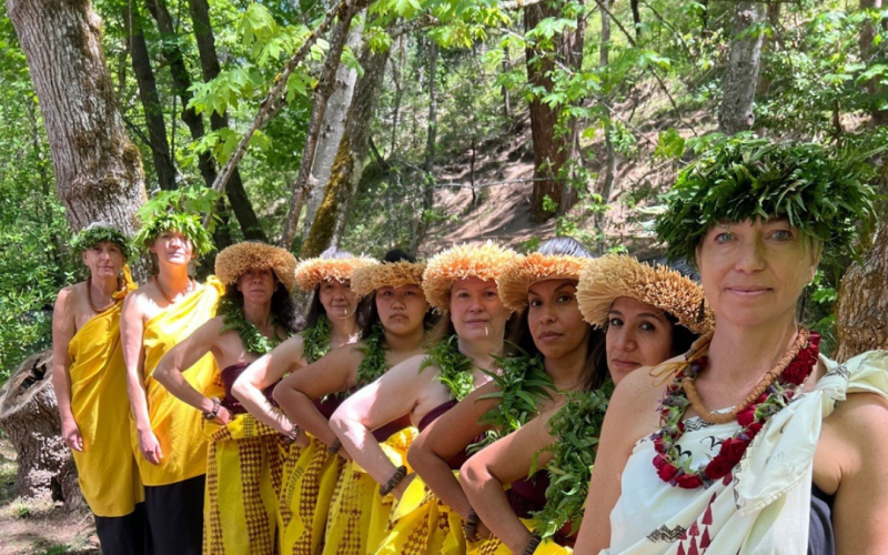 Andrea is standing in front of her students. She is wearing white and the students are wearing yellow.