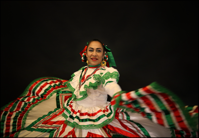 Kenya Marquez demonstrates traditional mexican folk dancing, wearing a long skirt with the colors red, white, and green.