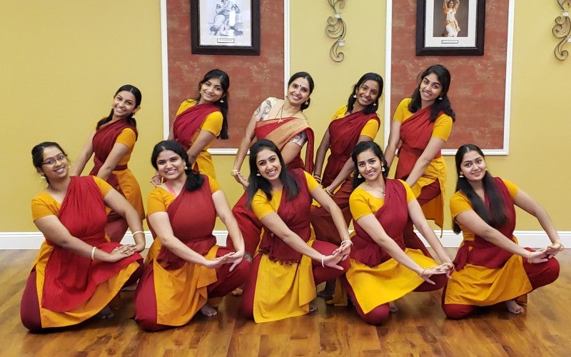 10 dance apprentices posing with Anuradha in red and yellow salwar kamiz