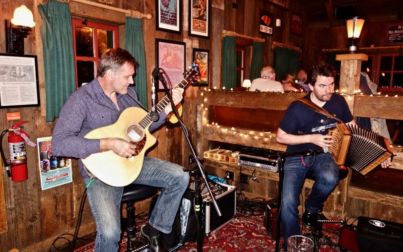 Johnny B. Connolly sits and plays next to a man playing a guitar.