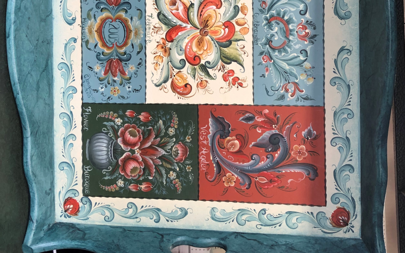 A blue, red, and white sampler tray showing 7 Rosemåling styles.