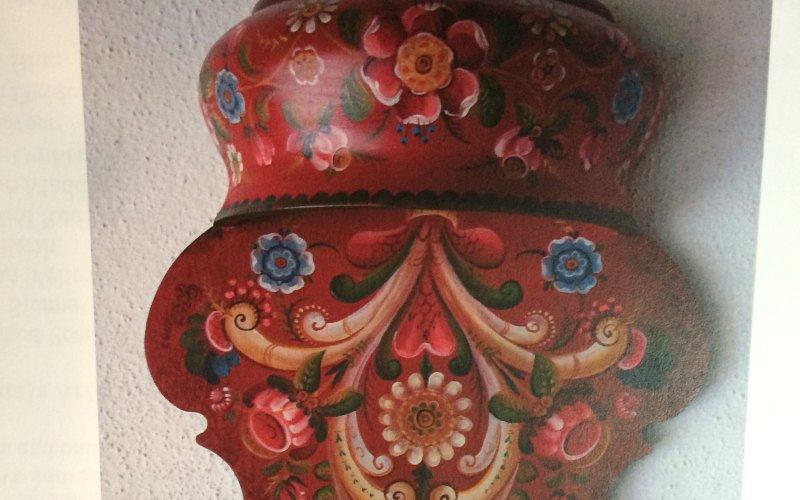 A red and multicolored decoration with floral Rosemåling, described as a study of roses from Osterdallen, Os, and Valdres.