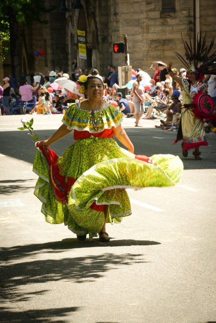Luisa Valentin Pelagio walking in a parade and swirling her folklorico dance costume. Her folklorico dance costume is yellow and red.
