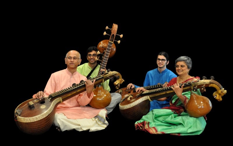 Sreevidhya Chandramouli and three indian men sitting against an all black background. They are all holding veena instruments.