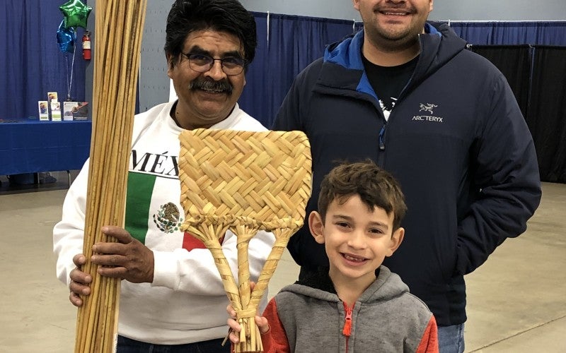 Dagoberto with his son Nick Morales and child from the event in Roseburg. Dagoberto is holding a bundle o tule and the child is holding a woven tule fan.
