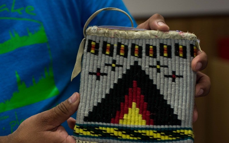 Michael Johnson holding a tan woven bag with red, blue, and yellow embroidered details.
