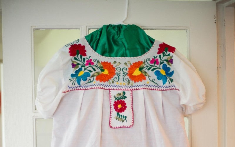 A white, red, and green ballet folklorico dress on a hanger. It is hanging off of a door.