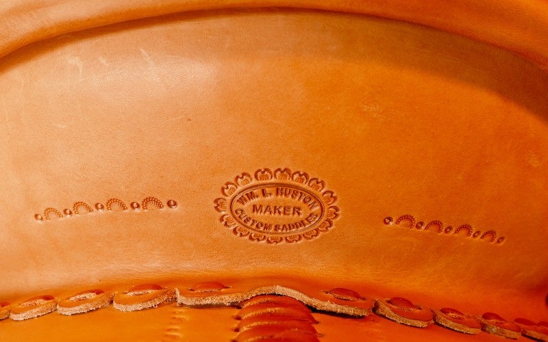 A close up shot of an orange piece of leather containing a circular brand imprint saying "WM. L. HUSTON MAKER CUSTOM SADDLES."