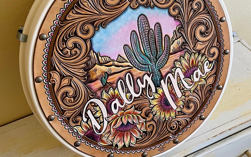 A brown leather piece with sunflowers, desert landscape, and the words Dally Mae