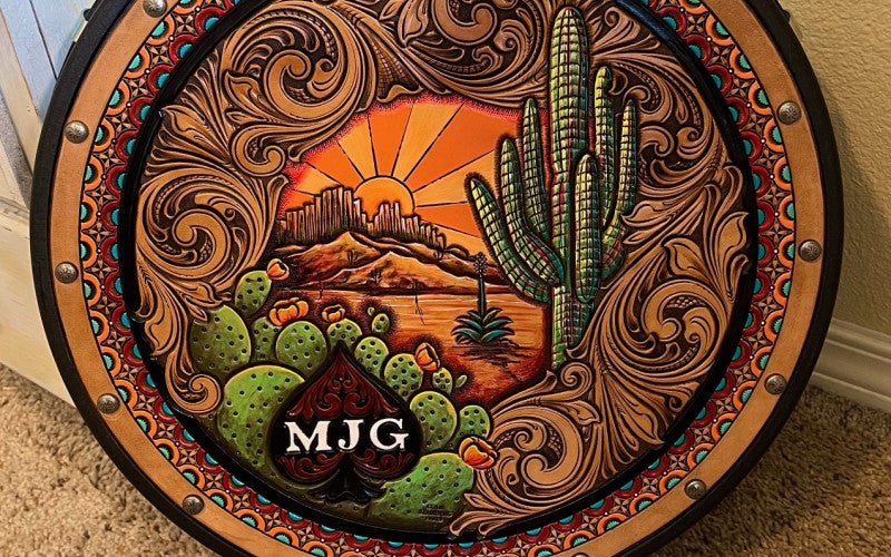 Brown leather piece with desert landscape, cactuses, and the letters MJG