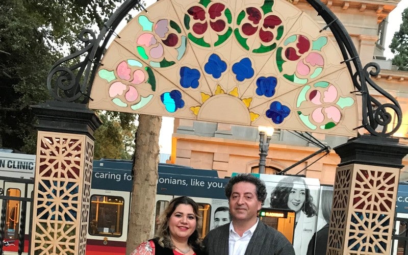 Photo of Houshang Sedighi and a women wearing Kurdish attire outside under an arch.